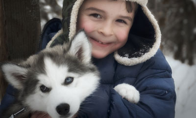 Boy hugging husky puppy in snow